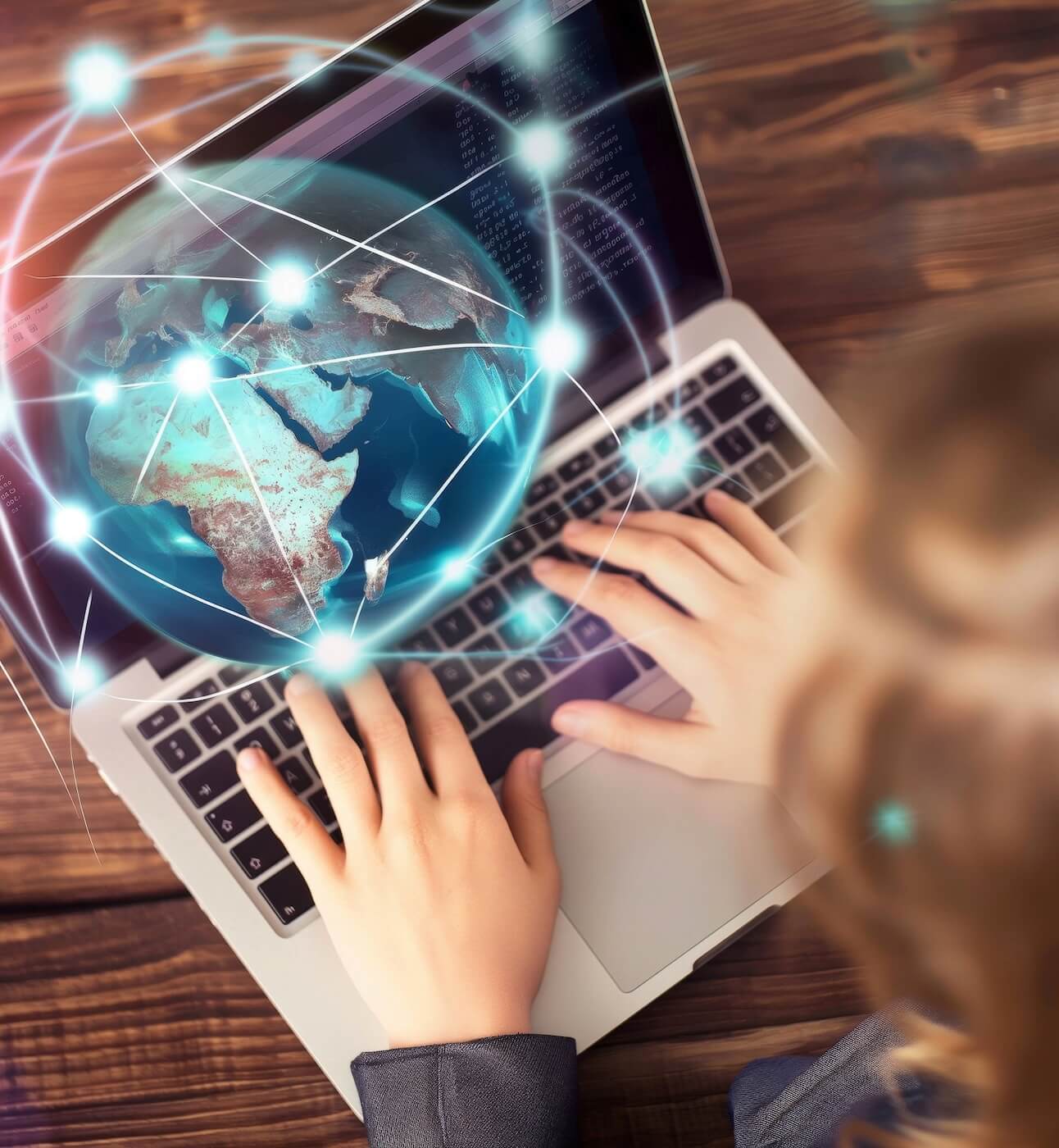 We are looking down on a woman typing on a laptop. There is a globe hologram with a network of connected lines and dots hovering over the laptop.