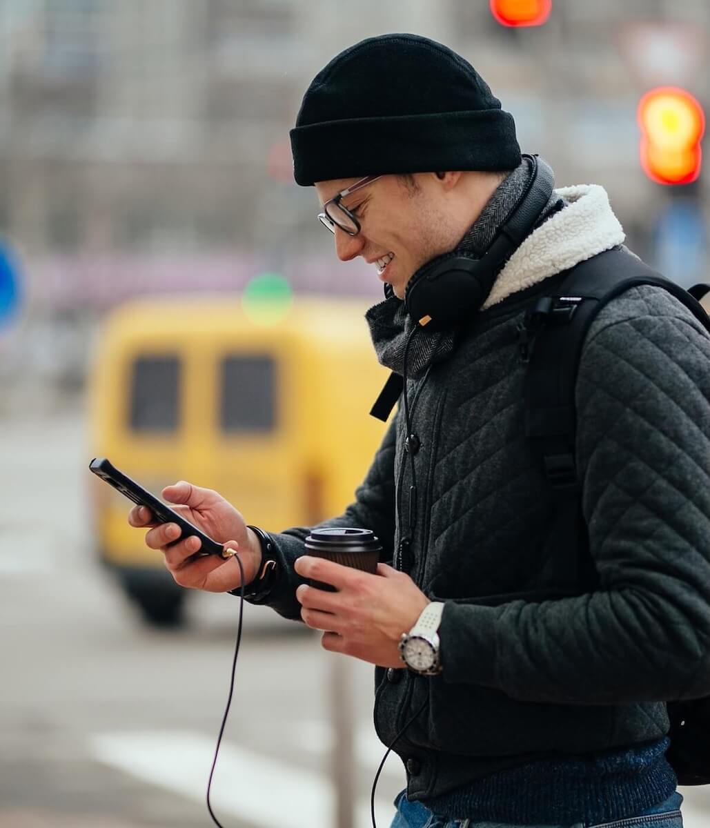 A man is walking down the street wearing a black hat and quilted black jacket. He is on his cellphone, using Newshosting’s VPN to keep his personal information safe.