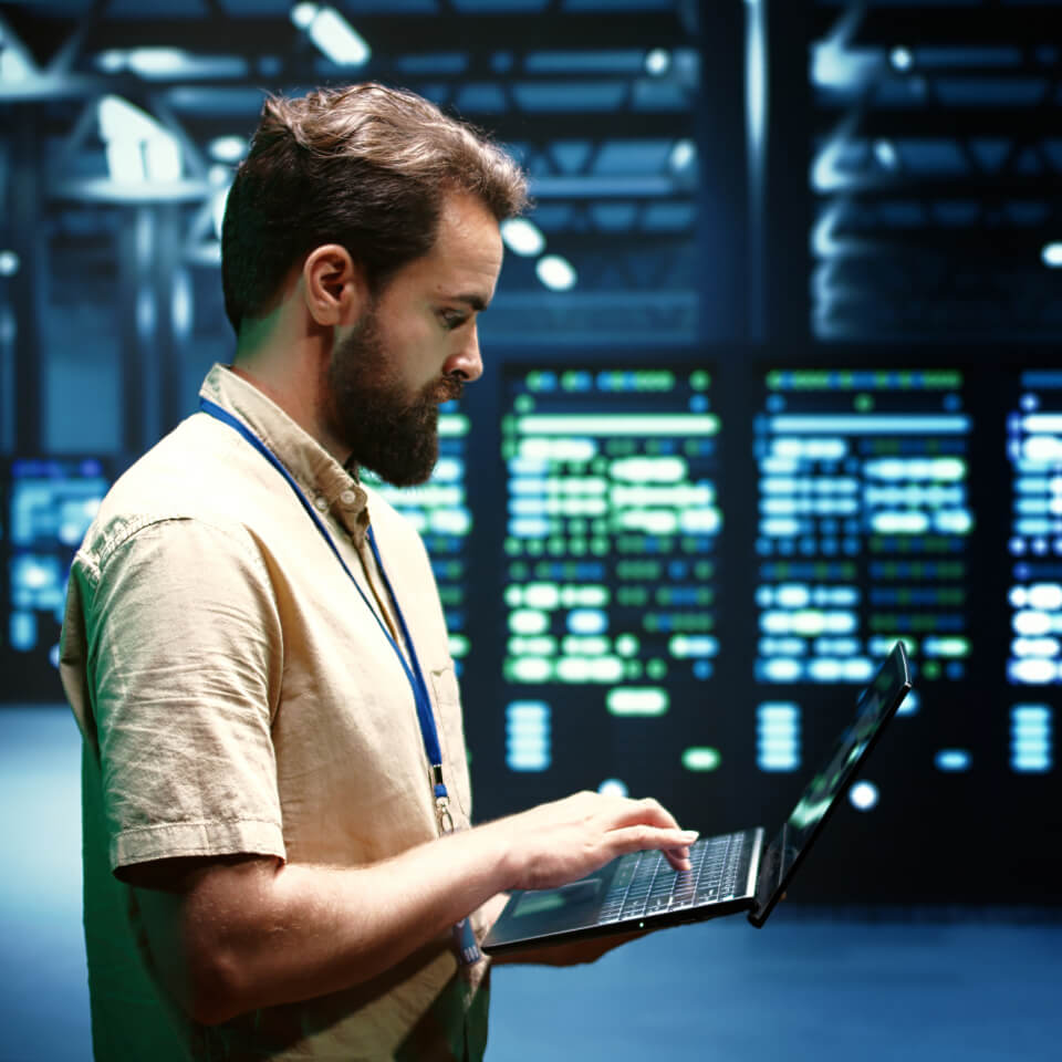 A professional technician is holding a laptop in a data center with one hand while typing with the other hand to optimize the Newshosting network.