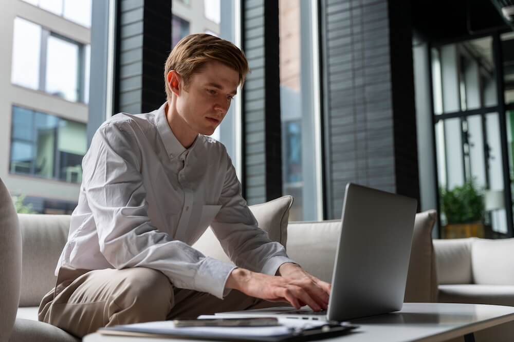 A man in a beige buttondown shirt and slacks is typing on a laptop.