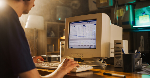 A man on an older computer is looking at a spreadsheet in a Windows ‘95 version of Excel.